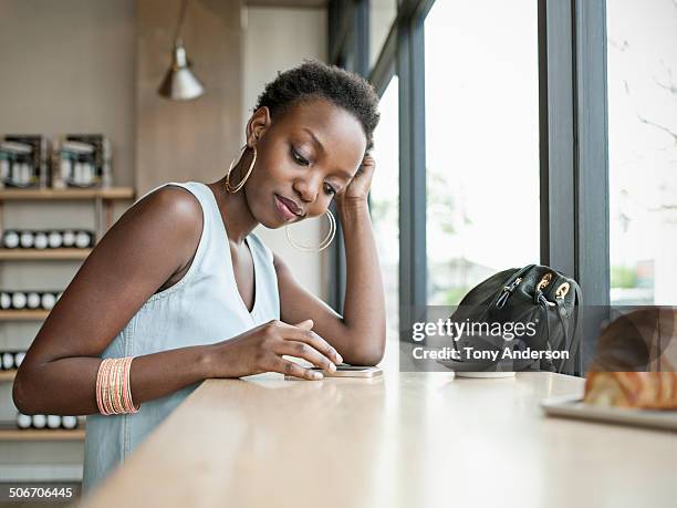 young woman in café with mobile phone - african american restaurant texting stockfoto's en -beelden