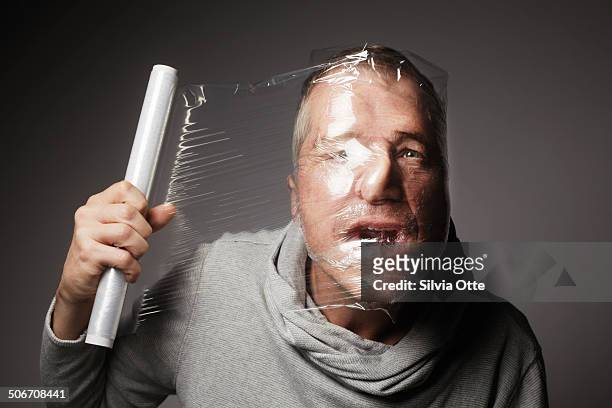 adult male wrapping his head in cellophane - man wrapped in plastic stock pictures, royalty-free photos & images