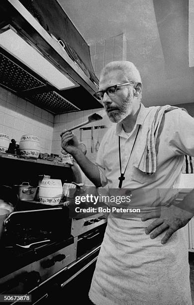 Episcopal minister & author-chef Father Robert F. Capon cooking on restaurant-size gas stove in kitchen of rectory.