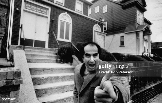 Comic face made by author, Philip Roth, while standing near Jewish center and Hebrew school he probably attended as a boy.