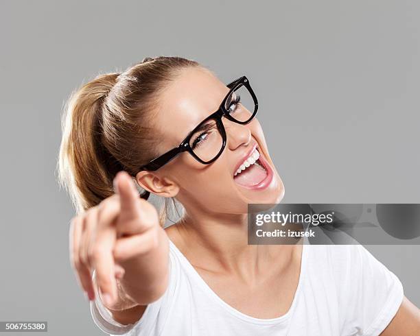 happy blonde young woman pointing at camera - happy face glasses stockfoto's en -beelden