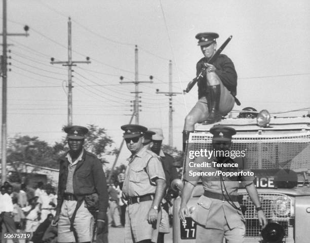 Policemen order local residents to clear the streets of debris after rioting broke out following a protest strike against the introduction of the...