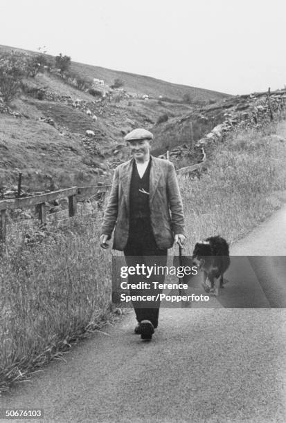Yorkshire farmer walks along a road with his Border Collie dog in the Swaledale valley area of the Yorkshire Dales National Park, England circa July...