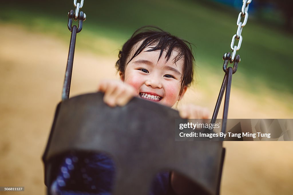 Child playing on swing joyfully in sand playground