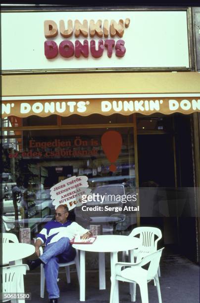Customer sitting at sidewalk table outside Dunkin' Donuts restaurant.