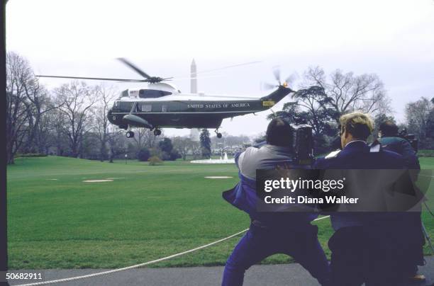 Cameramen fighting blast of wind ruffling their hair and clothing as President Ronald W. Reagan's copter lifts off from grassy spot with Washington...