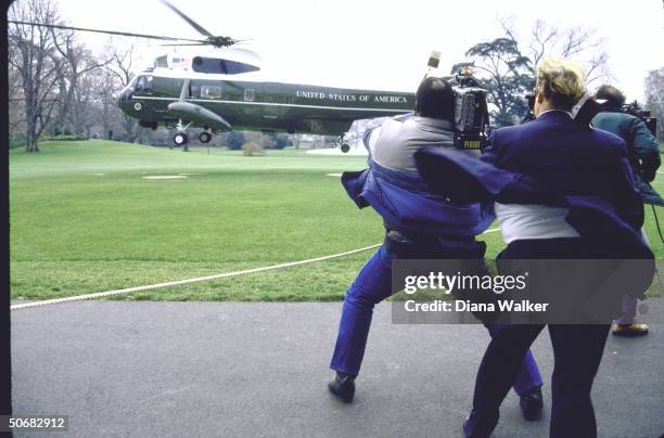 Cameramen fighting blast of wind ruffling their hair and clothing as President Ronald W. Reagan's copter lifts off from grassy spot as he leaves for...
