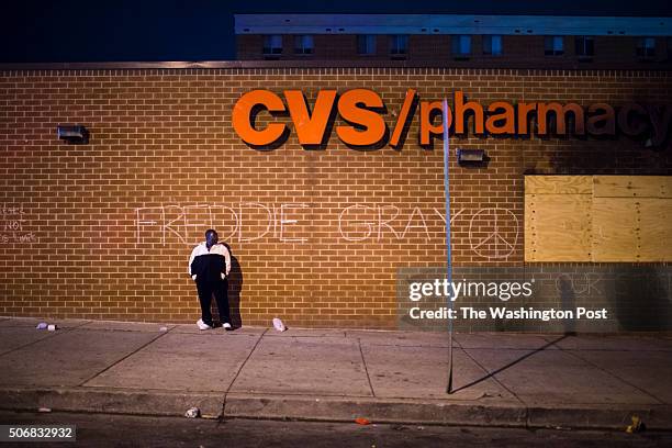 Man stands in front of the CVS Pharmacy that had been looted and burned Monday as people shout and block traffic as the 10 p.m. Curfew nears at the...