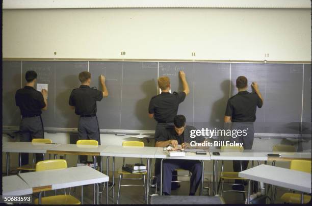 Four cadets working on math problems on blackboard.
