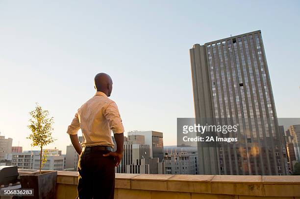 the rear view of a man look out from his balcony of a city apartment in johannesburg, south africa. - gauteng province stock pictures, royalty-free photos & images