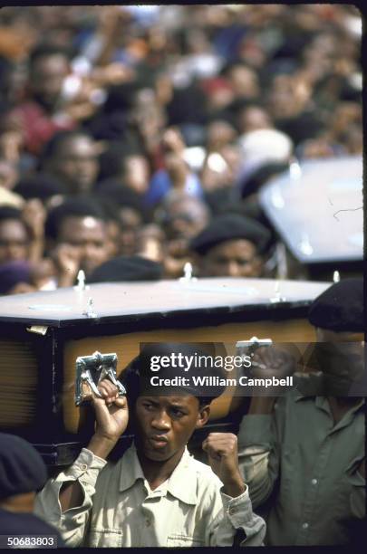 Mourners raise clench fists while carrying coffins through crowd during mass funeral of 18 blacks killed by police action during township unrest in...