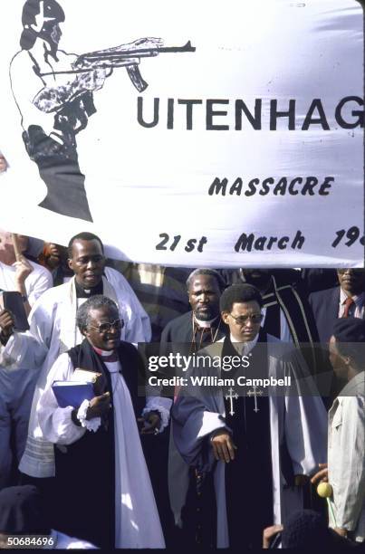 Bishop Desmond Tutu and Allan Boesak at funeral of 29 killed in unrest, anti-government sign in background.