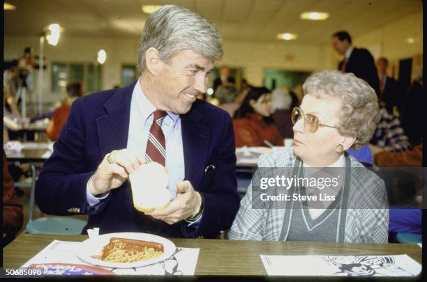 At AARP spaghetti dinner during presidential campaign, NY Repub. Rep. Jack Kemp sitting at table holding piece of bread and giving older woman flirty...