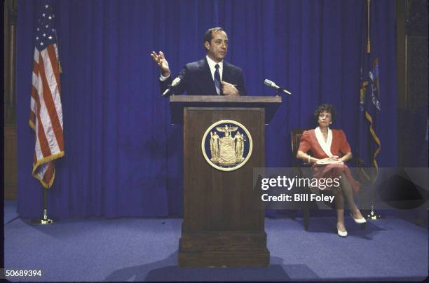 Governor Mario Cuomo at podium with state seal as he annouces he will seek re-election, with wife Matilda seated at right.