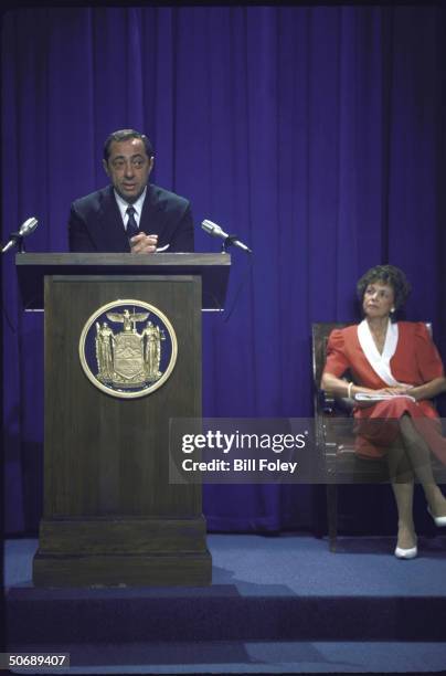Governor Mario Cuomo at podium with state seal as he annouces he will seek re-election, with wife Matilda seated at right.