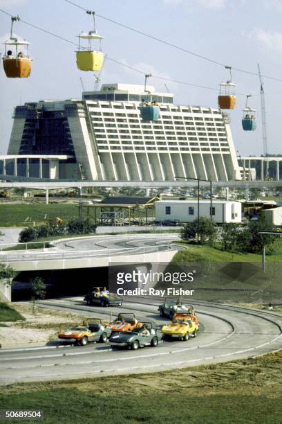 Disneyworld's Skyway multicolored cable cars passing over the raceway with futuristic hotel in the background.