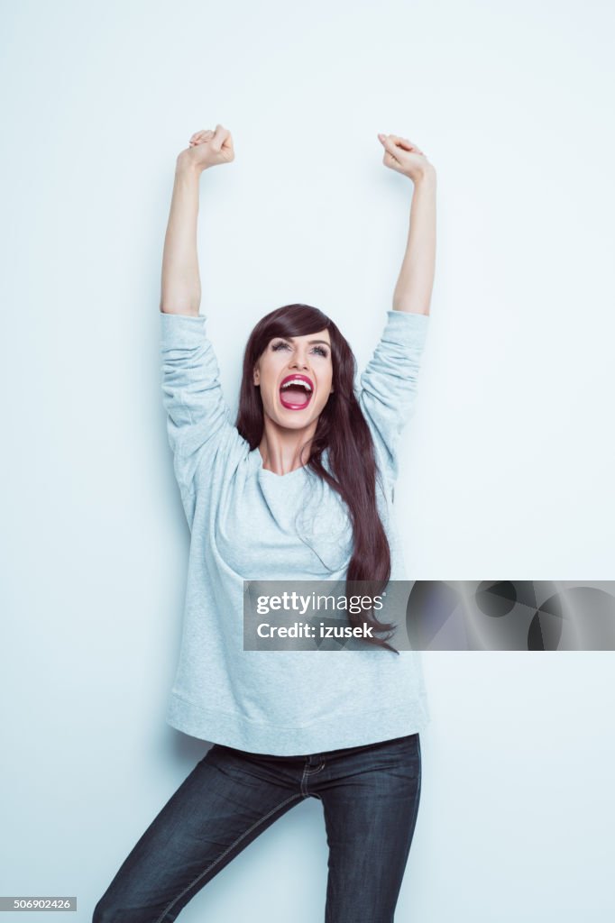 Excited brunette in casual outfit, raising arms and shouting