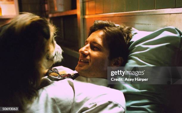 David Duchovny, co-star of cult TV series The X-Files, lying on bed w. Pet dog on the set of the show.