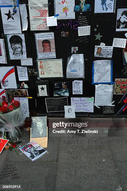 Gone but never forgotten our hero" is written on the pavement below posters, drawings and letters are mounted on a wall to the right of the flowers...