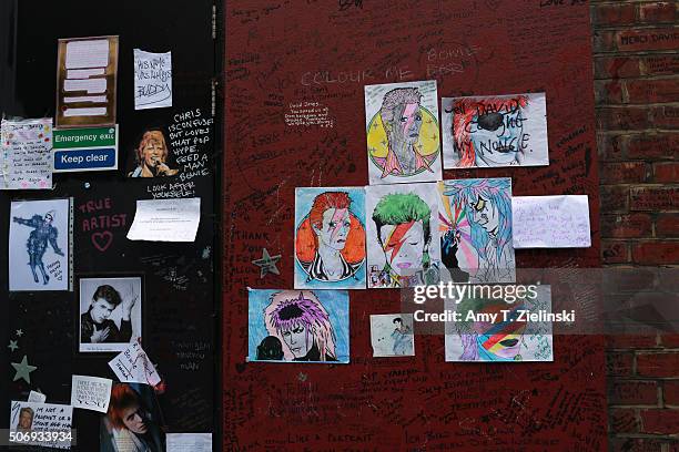 Posters, drawings and letters are mounted on a wall to the right of the flowers and other items left on a mound that continues to grow two weeks...
