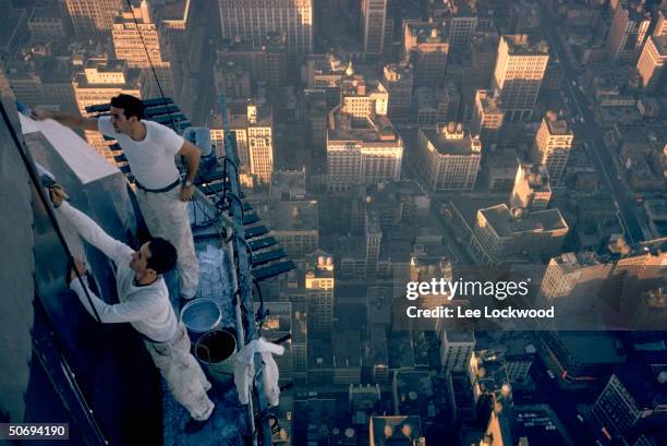 Workmen cleaning exterior of Empire State Building with bird's-eye view of city in background.