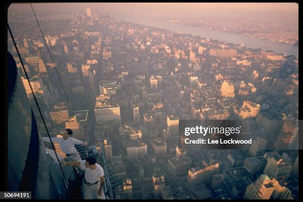 Workmen cleaning exterior of Empire State Building with bird's-eye view of city in background.
