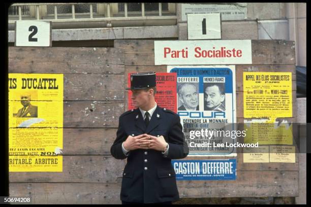 Gendarme standing in front of French election posters promoting socialist party candidates including Pierrre Mendes-France.