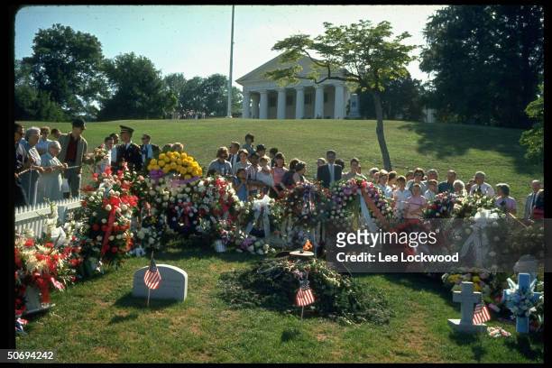 Visitors at grave site paying respects to slain President John F. Kennedy on first birthday after the assassination as military guard stands by.