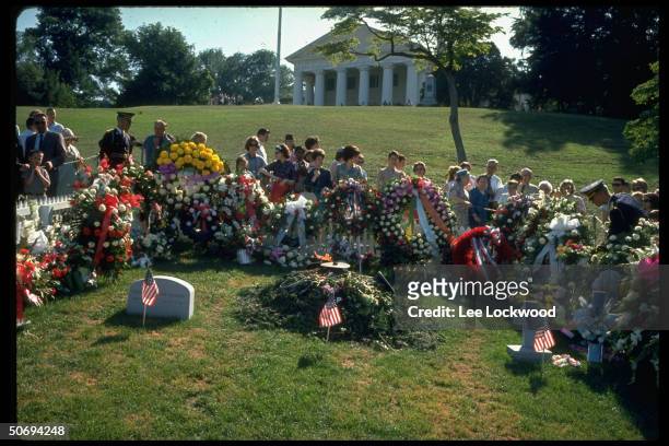 Visitors surrounding grave site paying respects to slain President John F. Kennedy on first birthday after assassination as military guards stand by.