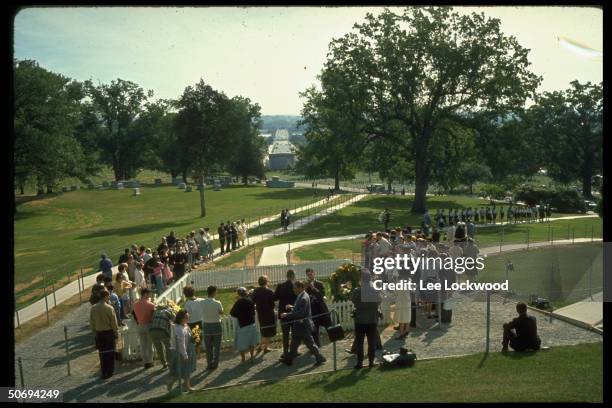 Visitors lining up and surrounding grave site pay respects to slain President John F. Kennedy on first birthday after the assassination as military...