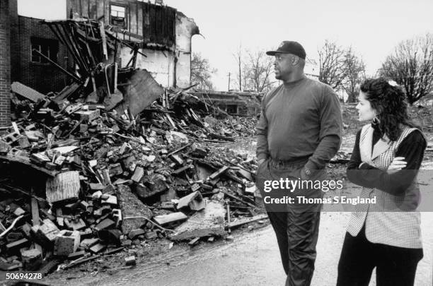 Pro football player Reggie White & wife Sara walking past burnt rubble of Inner City Church, where he acts as asst. Pastor, re growing epidemic of...