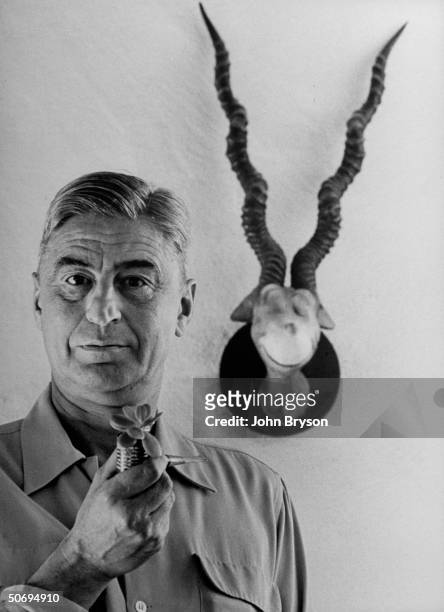 Children's book author Theodor Seuss Geisel holding favorite plant-sprouting corncob pipe as he stands in front of his 1940 sculpture of the...