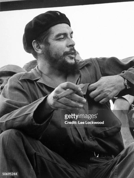 Che Guevara , Cuban hero, sitting on viewing stand smoking big cigar at July 26th celebration of the revolution.