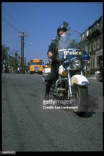 Helmeted policeman on motorcycle escorting students to newly integrated high school in South Boston during crisis precipitated by busing law.