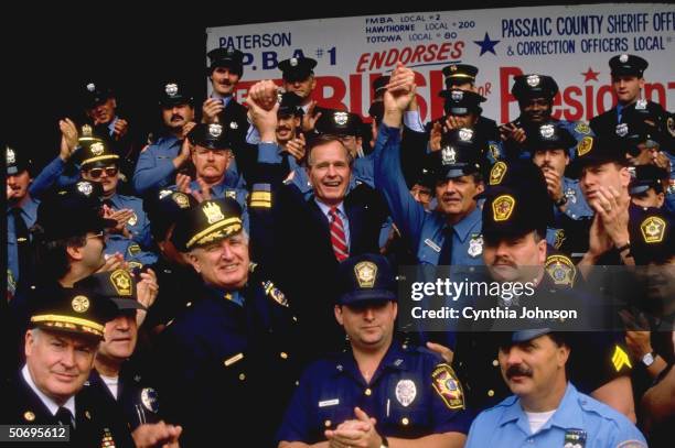 Republican presidential candidate VP George Bush raising linked hands w. 2 of crowd in blue, being endorsed by Passaic County Police Benevolent Assoc.
