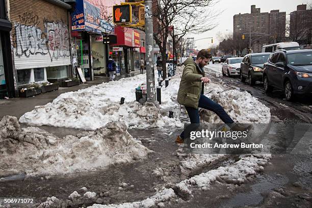 Man attempts to step over slushy snow and puddles while crossing the street on January 26, 2016 in New York City. The city is still recovering from a...