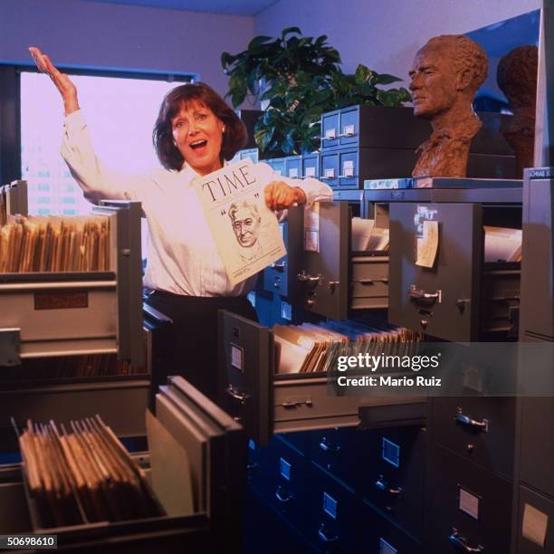 Archivist Elaine Felsher, retiring after 27 yrs., throwing up her arm amid her office files, w. 1922 TIME 1st pre-issue & Jo Davidson bust of Henry...