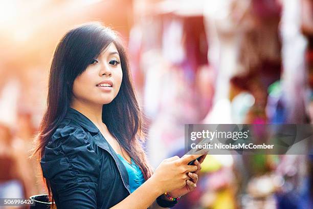 beautiful indonesian woman interrupts her text messaging - indonesia street market stock pictures, royalty-free photos & images