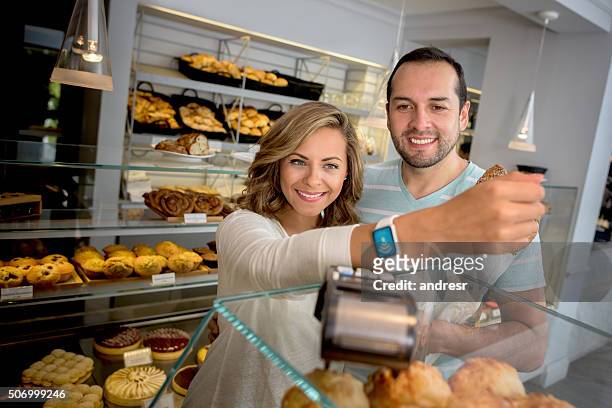 couple making a contactless payment at the bakery - watch payment stock pictures, royalty-free photos & images