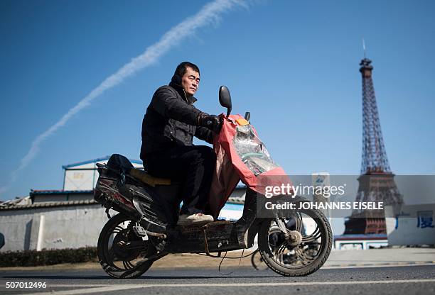 This picture taken on January 26, 2016 shows a man riding his motorbike past a replica of the Effel Tower in Tianducheng, a luxury real estate...