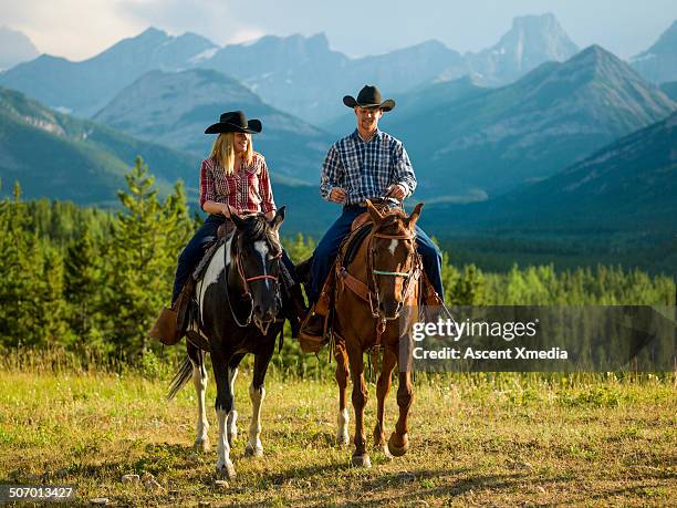 cowboy and cowgirl ride horse thru mountain meadow - cowboy riding stock pictures, royalty-free photos & images