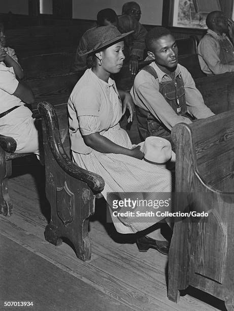 Male and female African-American farmers sitting in pews at a church during a Farm Security Administration meeting of borrowers in a church near...