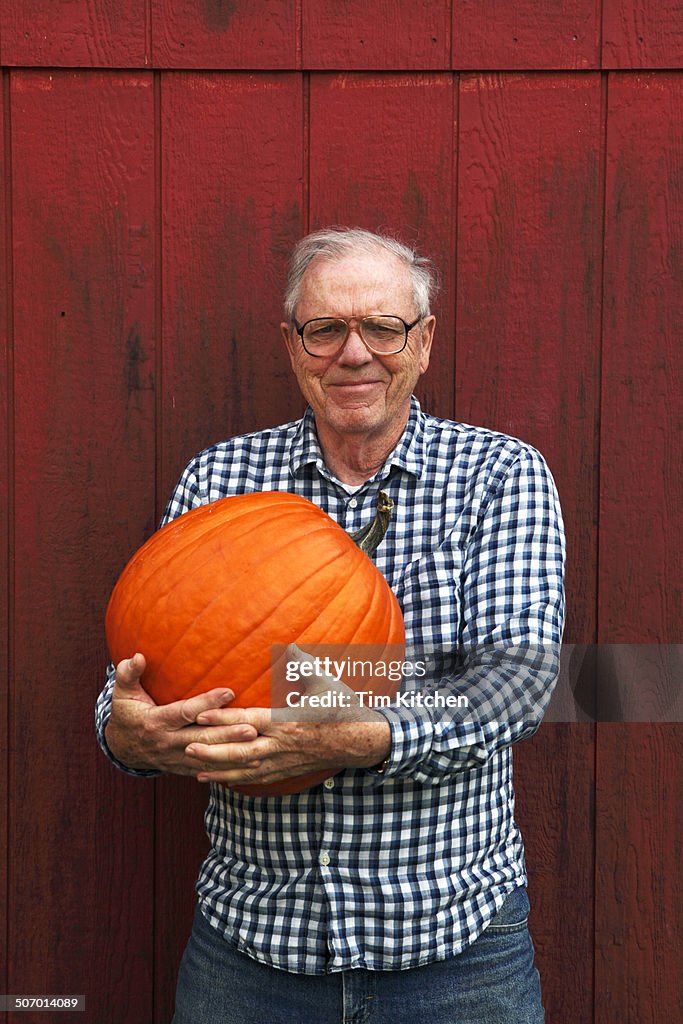 Elderly man holding pumpkin beside barn