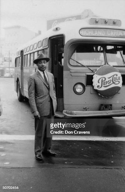 American religious and Civil Rights leader Reverend Dr Martin Luther King Jr stands in front of a bus at the end of the Montgomery bus boycott,...