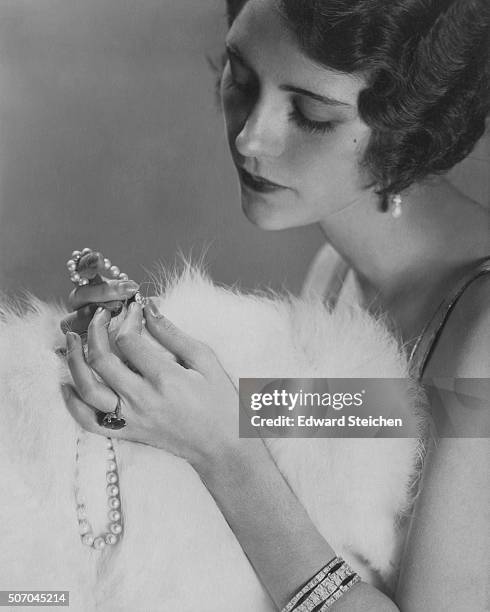 Close-up of Kendall Lee holding a pearl necklace and wearing a diamond bracelet and a sapphire ring with diamond baguettes, from Cartier; her hands...