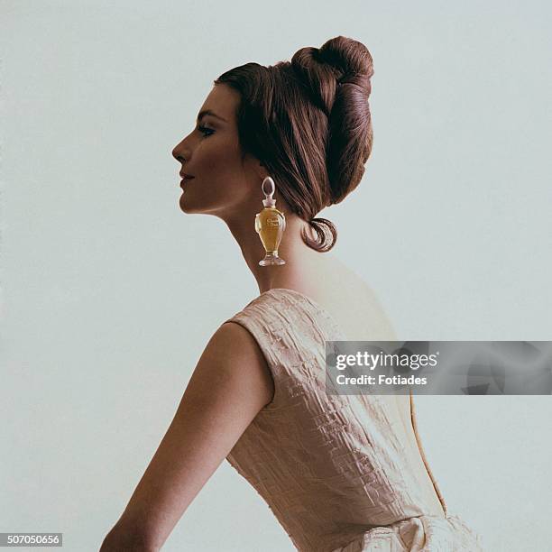 Profile view of a model wearing a bottle of Diorissimo by Dior perfume bottle as an earring.