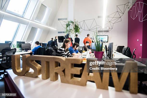 Logo sits on a desk area as employees work at laptop computers beyond, inside the Ustream, Inc. Office in Budapest, Hungary, on Tuesday, Jan. 26,...