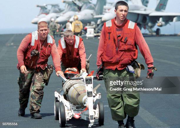 Aviation Ordnancemen assigned to the Shrikes of Strike Fighter Squadron Nine Four moving a laser guided bomb across the flight deck of the aircraft...