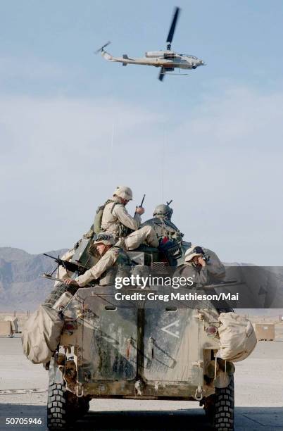 Marines on a Light Armored Vehicle preparing to go on patrol as an AH1W Super Cobra helicopter flies by. US Marines are in Afghanistan operating in...