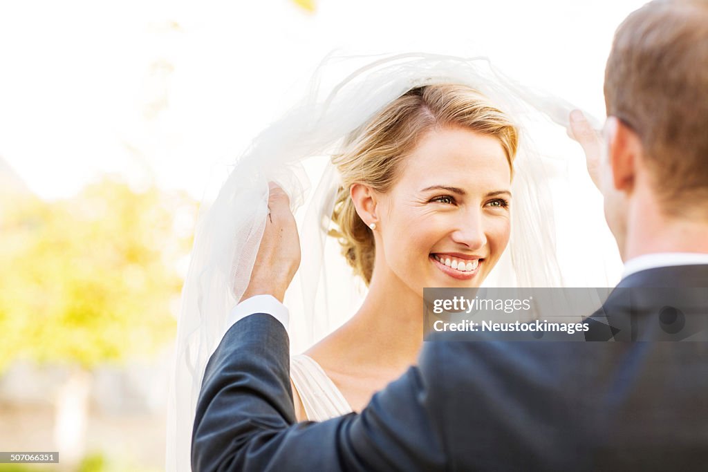 Glückliche Braut und Bräutigam beim wegsehen, während Ihr Schleier